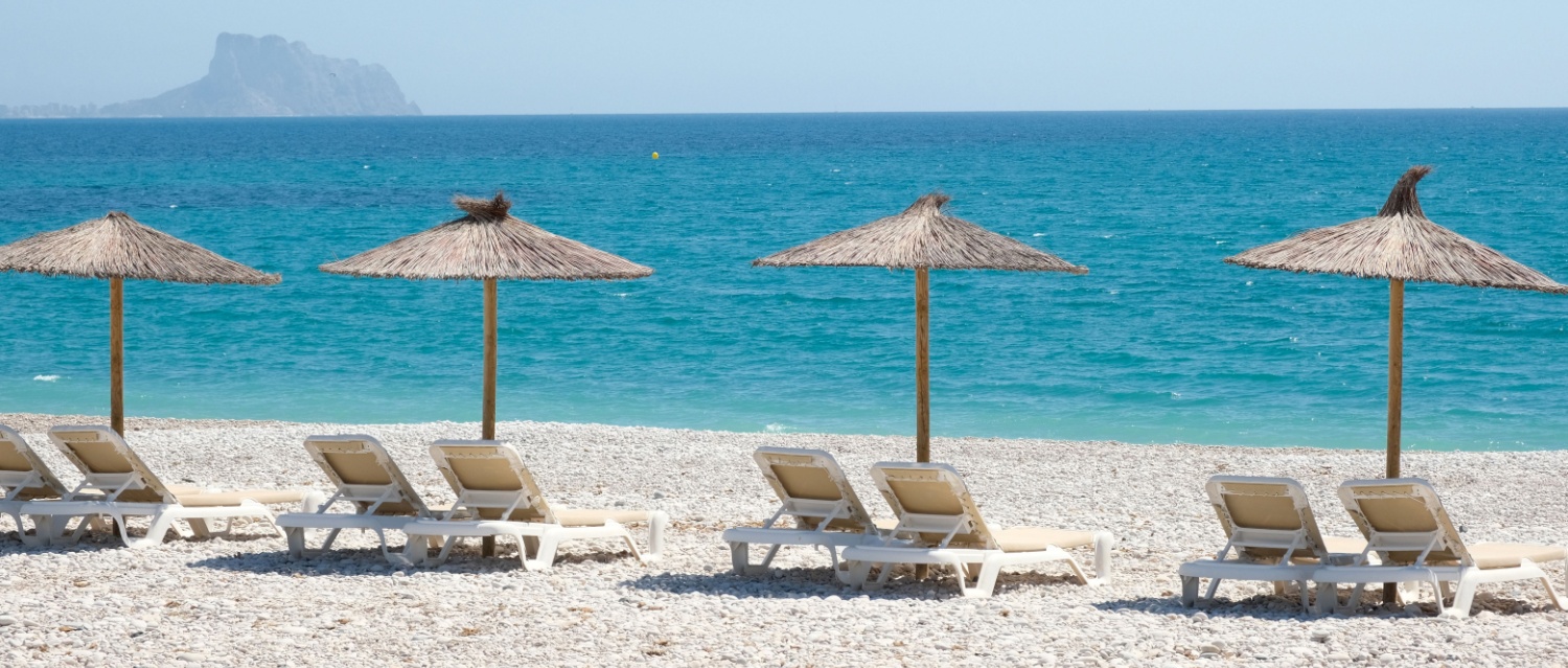 View to turquoise blue Mediterranean Sea and Albir seaside beach in Alicante province, Spain. Raco de Albir Beach with white pebbles, umbrellas.