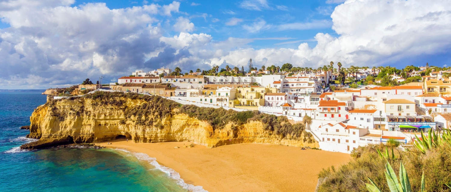 Wide sandy beach, white houses, cloudy sky with seagulls, Carvoeiro, Algarve, Portugal