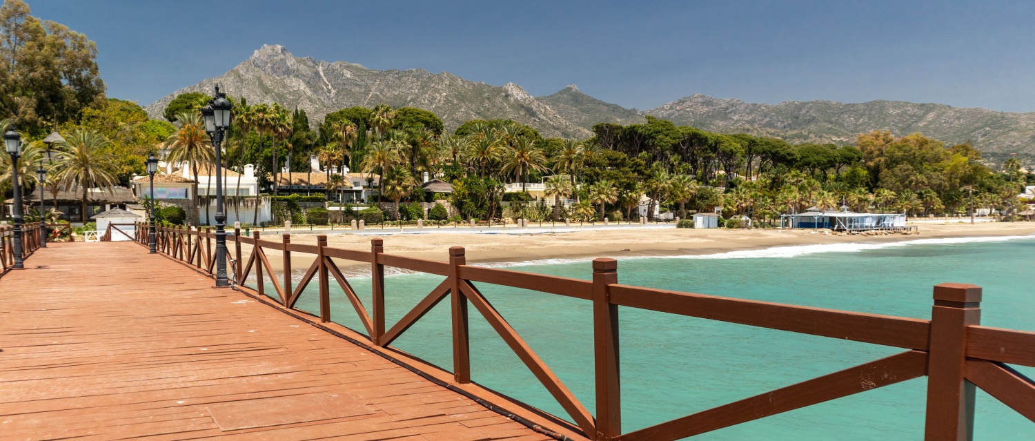 View of red wood bridge "Embarcadero" in Marbella. View of Luxury area Puente Romano, expensive urbanisations. Mountain "La Concha". Spectacular travel destination. Emerald water, no people