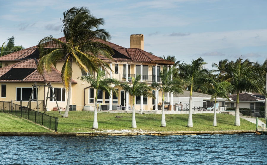 Large coastal home with a small boat tied to pier. Modern luxury waterfront real estate in Florida.