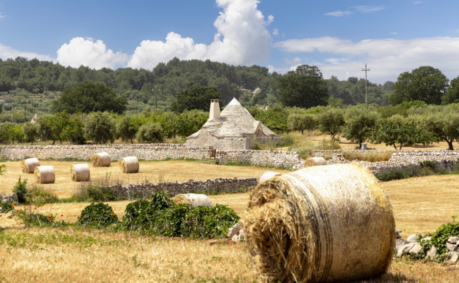 Picturesque view of the farm field after harvest, large straw bales and a trullo cottage, Itria Valley (Valle d'Itria), Italy, Apulia. Typical rural landscape of the Puglia region