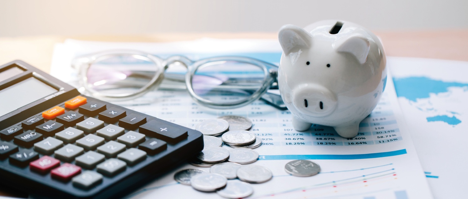 A calculator and piggy bank next to a pile of savings